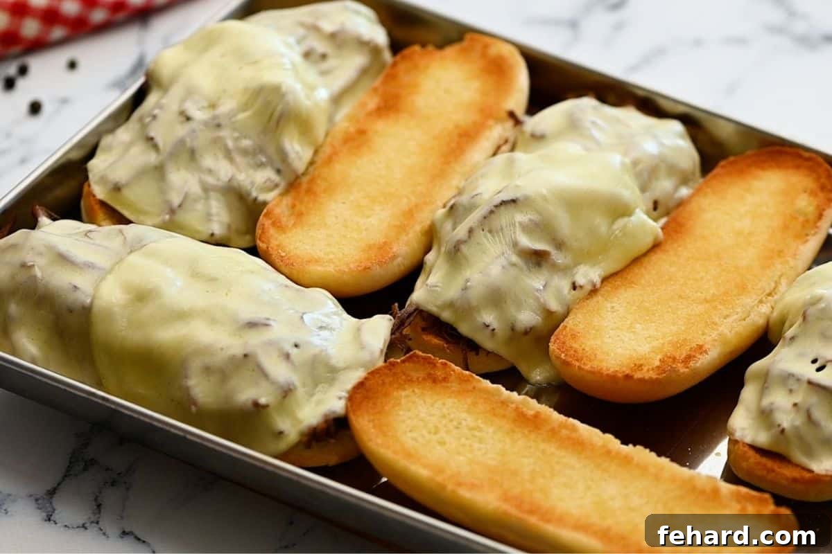 Toasted hoagie buns on a sheet tray topped with perfectly shredded Instant Pot French Dip beef and provolone cheese, ready for melting.