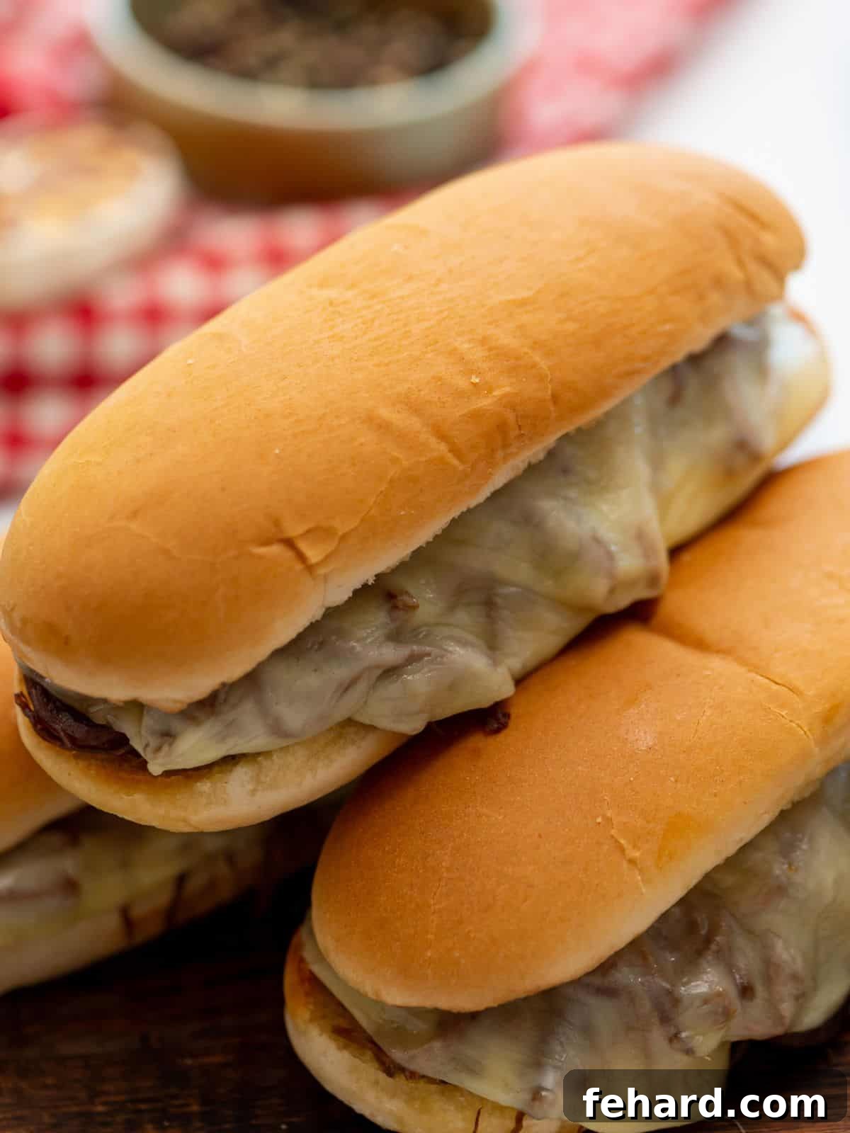 Assembled beef and provolone sandwiches on toasted buns, presented on a cutting board, ready to be served with au jus.