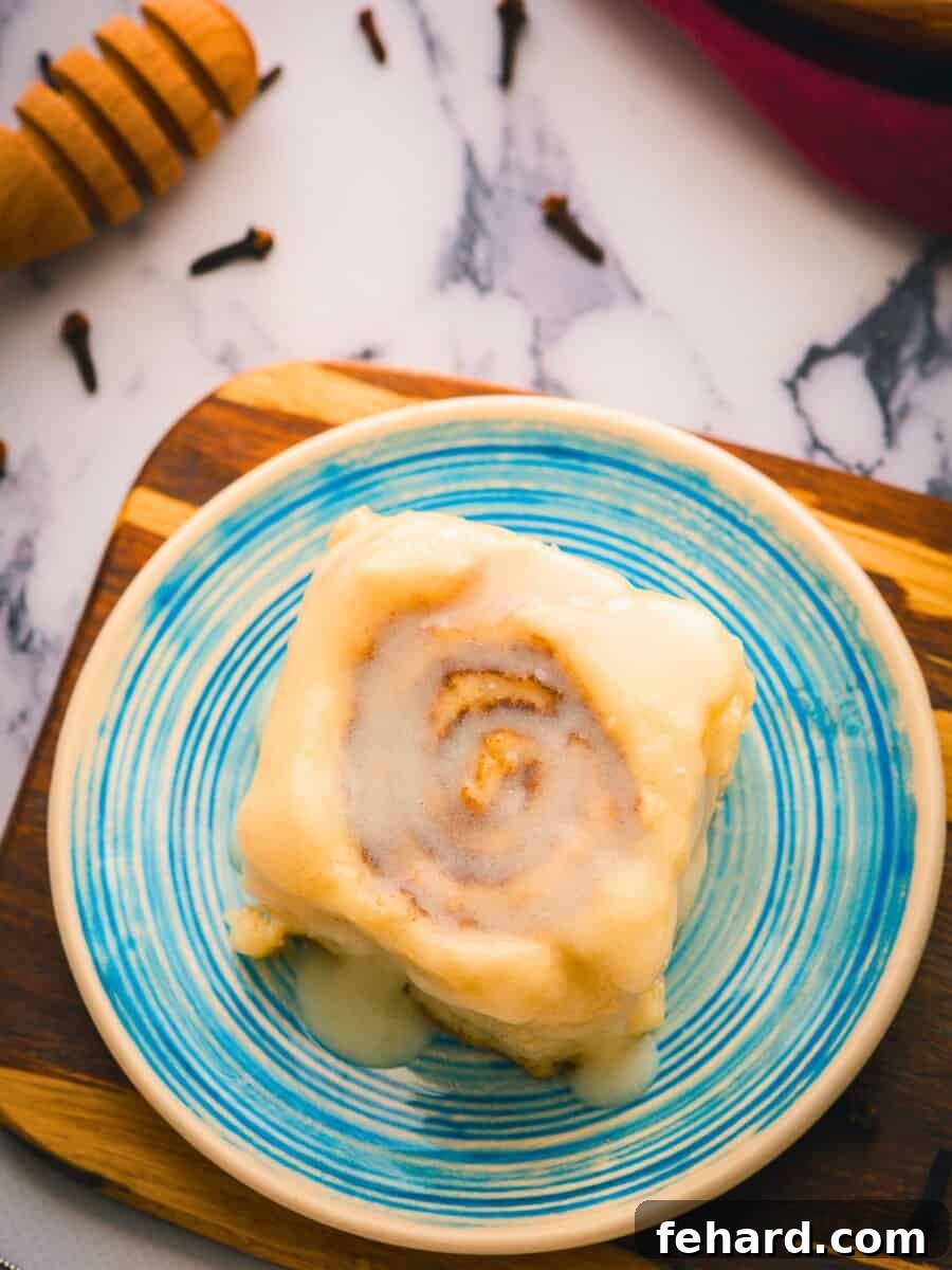 A fluffy homemade cinnamon roll made with bread dough and overnight preparation on plate with cream cheese glaze.