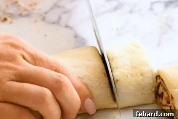 Knife cutting log of cinnamon roll dough into 9 rolls.