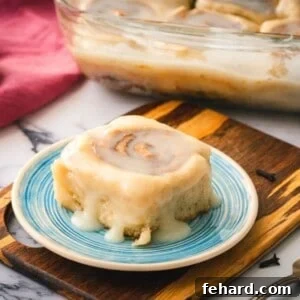 Healthy Cinnamon Roll on blue serving plate with tray of cinnamon rolls in background.