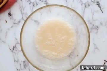 Yeast, honey, and water in mixing bowl with bubbles on surface.
