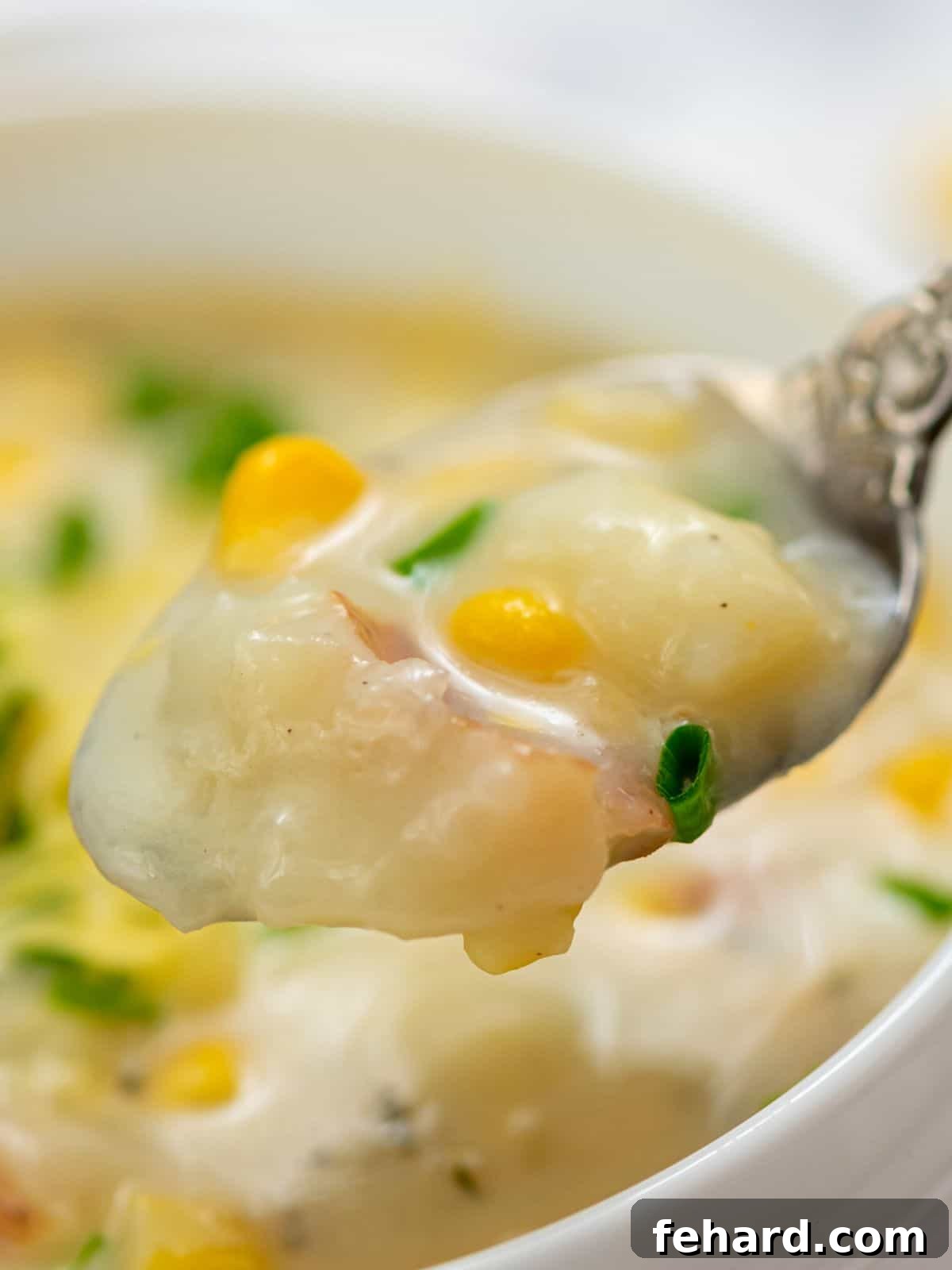 Spoonful of creamy potato corn chowder served with cheddar and chives, inviting and warm.