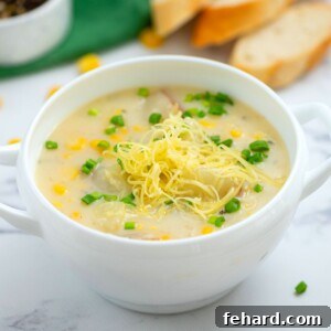 Bowl of Potato Corn Chowder topped with sharp white cheddar and chives, a comforting and flavorful dish.