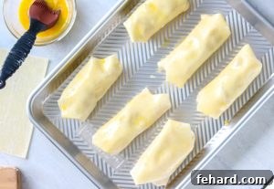Brushing egg rolls with egg wash on sheet pan