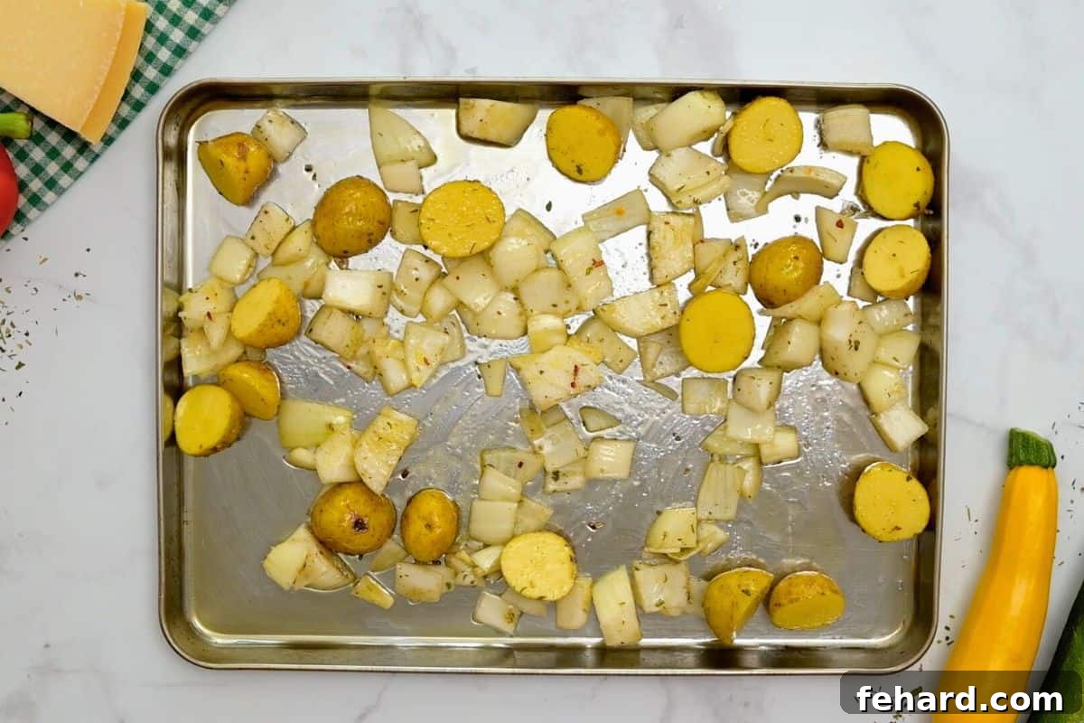 Initial Roast of Potatoes and Onions Seasoned and pre-roasted potatoes and onions evenly spread on a large rimmed sheet pan, showing early caramelization.