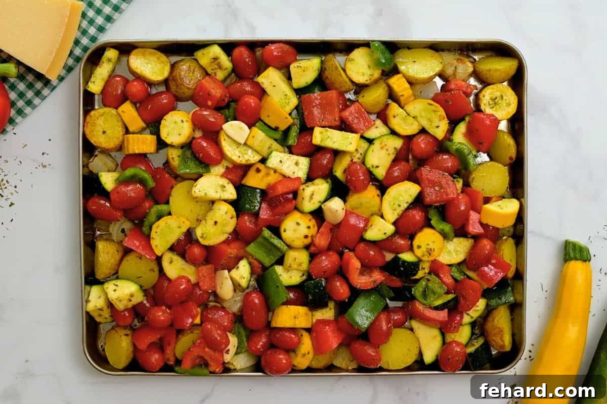 Adding More Vegetables for Roasting Italian seasoned peppers, squash, and tomatoes mixed with partially roasted potatoes and onions on a large rimmed sheet pan.