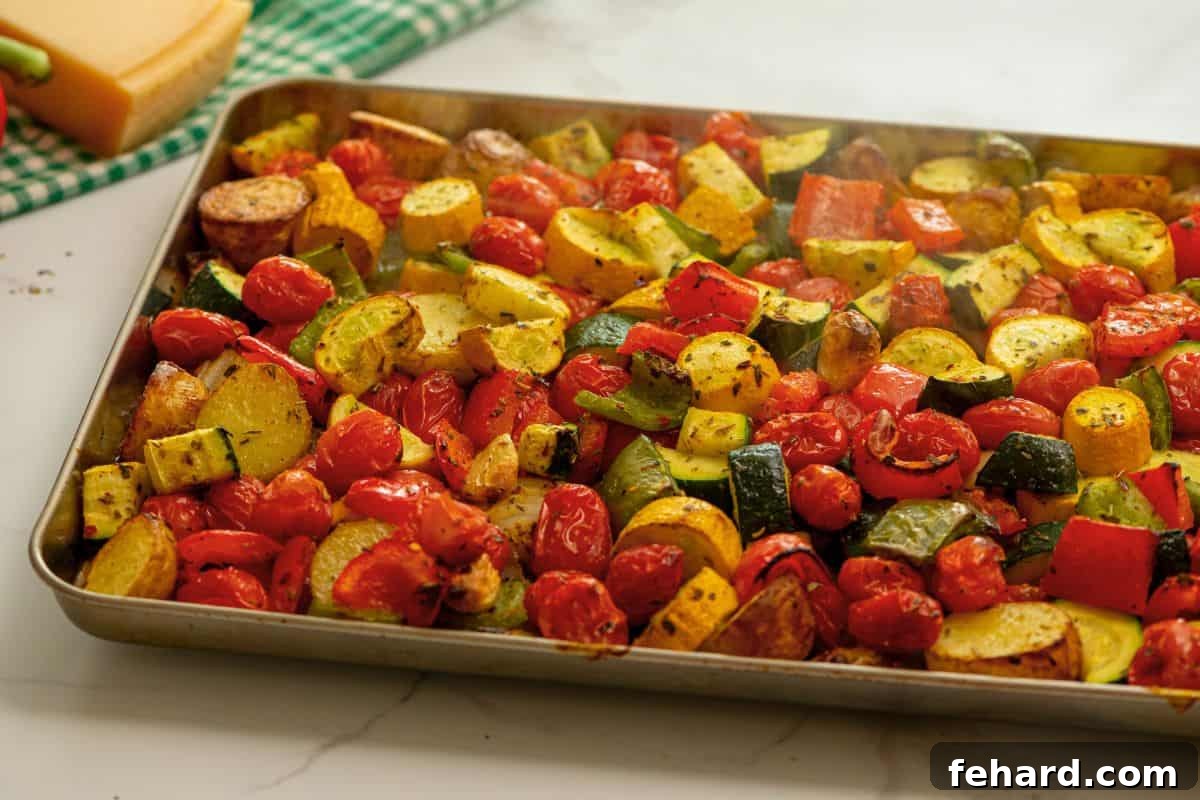 Finishing with Parmesan Cheese Roasted potatoes, squash, and tomatoes beautifully caramelized on a rimmed sheet pan, being topped with freshly grated parmesan cheese.