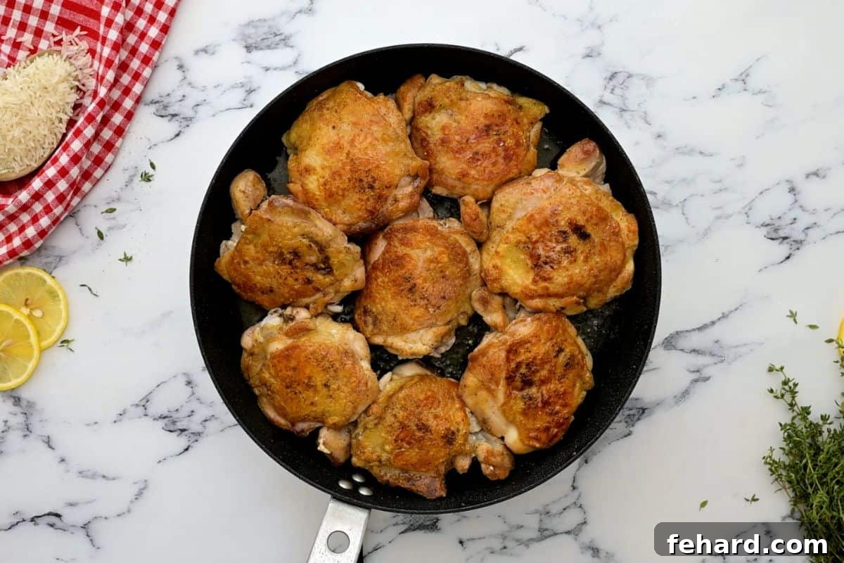 Perfectly seared chicken thighs with golden brown crispy skin in a large sauté pan, ready for the slow cooker.
