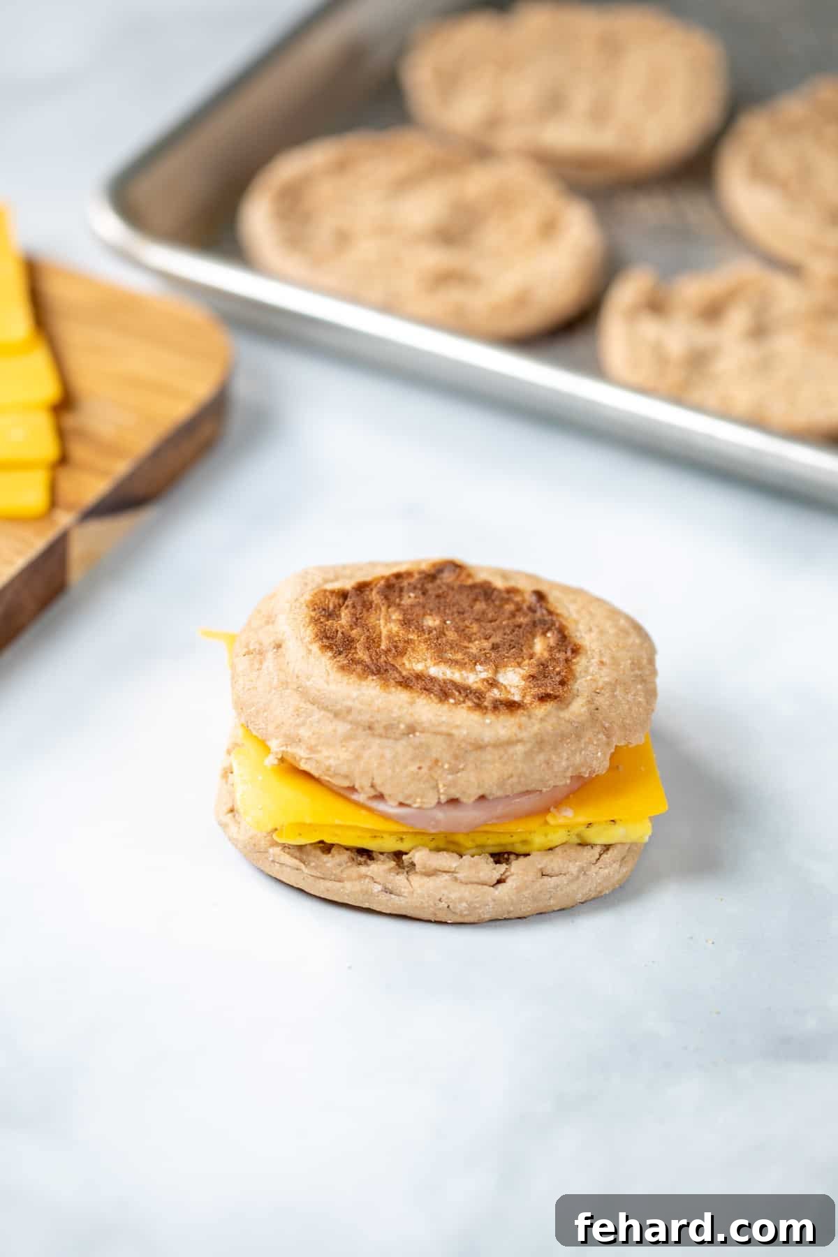 A freshly assembled Homemade Egg McMuffin, showcasing fluffy egg, melted cheese, and Canadian bacon, resting beside perfectly toasted English muffin halves.