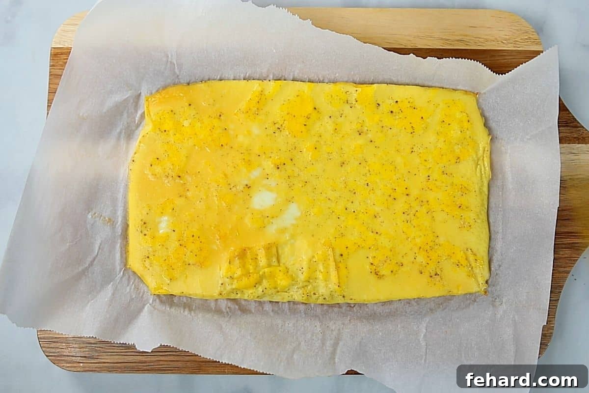A golden-brown sheet of baked scrambled eggs, perfectly set on parchment paper, resting on a wooden cutting board.
