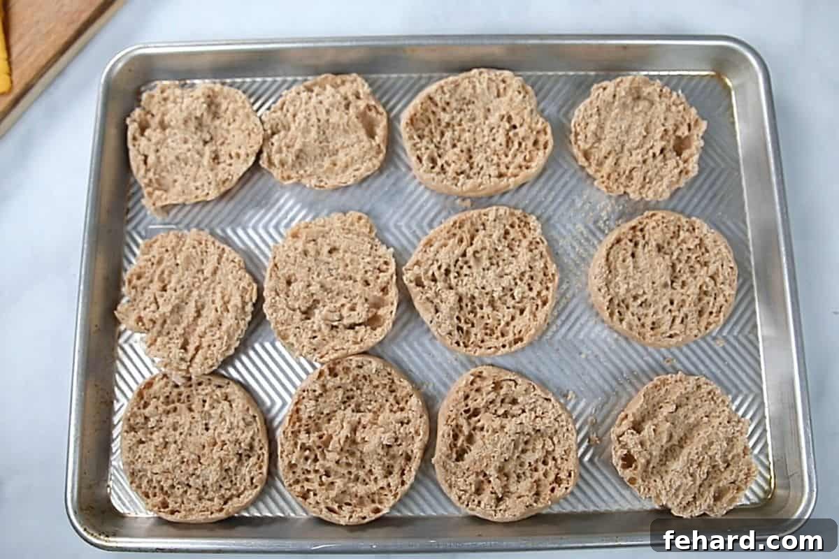 Perfectly toasted English muffin halves arranged on a baking sheet, ready for assembly into delicious breakfast sandwiches.