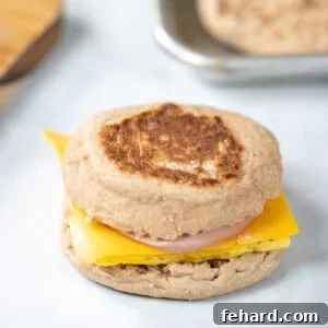 A copycat egg mcmuffin breakfast sandwich on counter with toasted English muffins in background.
