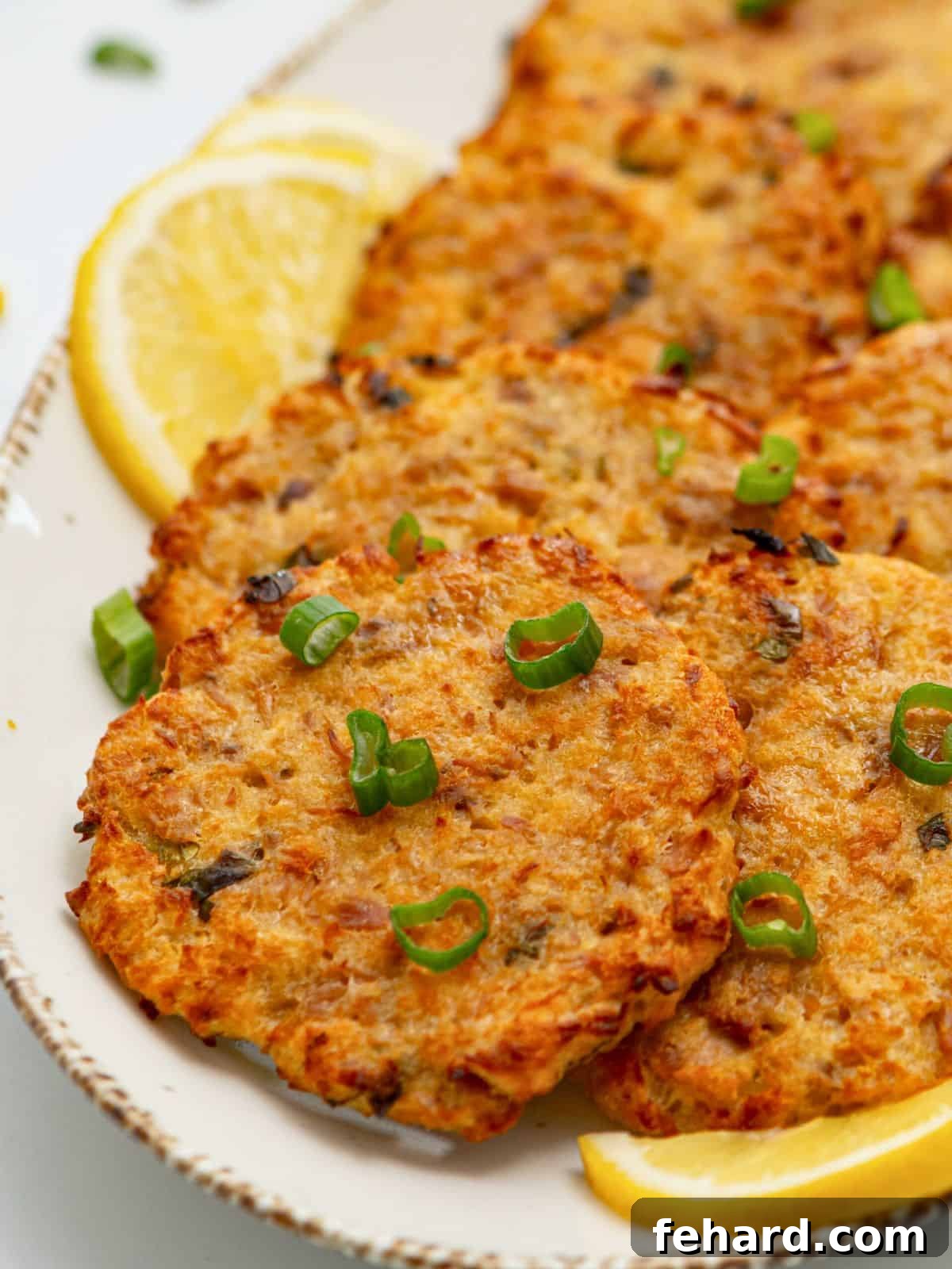 Baked crispy thin tuna patties on platter with lemon wedges and topped with green onions.