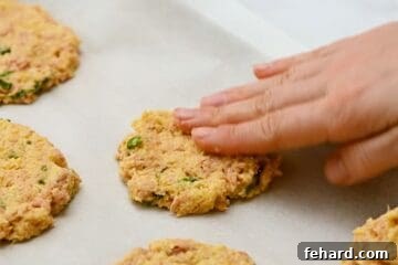Tuna patties on parchment paper lined baking sheet, with hand shaping into patties.