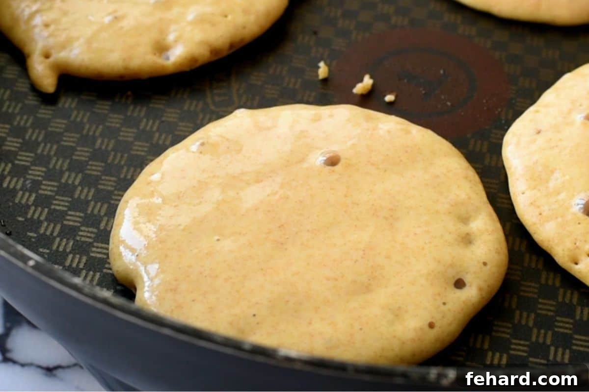 Whole Wheat Pancakes cooking in a skillet, showing tiny bubbles forming on the surface, indicating they are almost ready to flip.