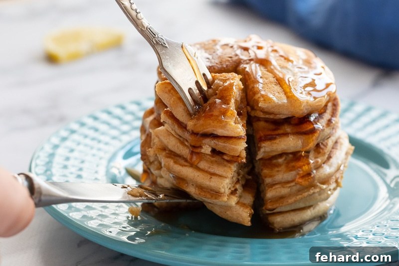 A stack of whole wheat pancakes on a plate, being cut into, revealing their fluffy interior.