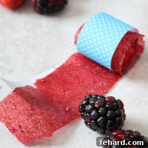 Real Fruit Delights: DIY Chewy Strips 3 A homemade fruit roll-up rolled up in blue craft paper with blackberries and strawberries to the side.