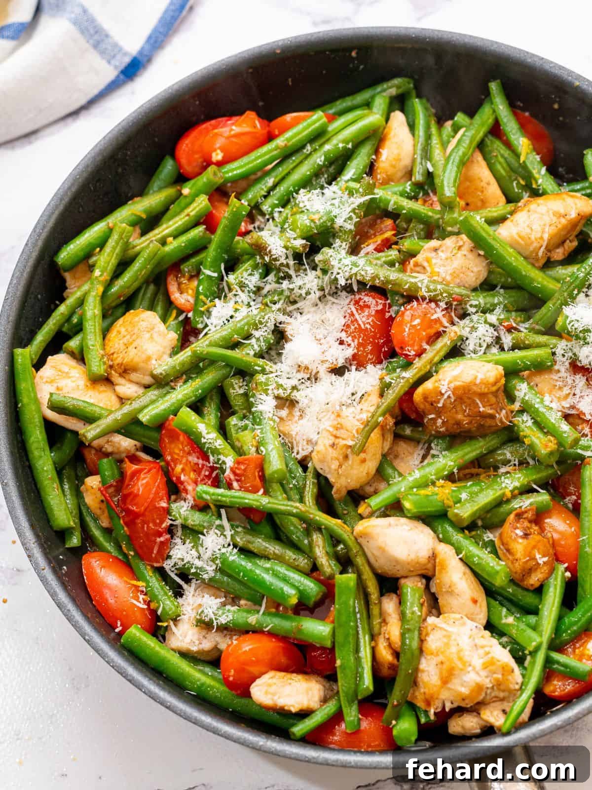 Chicken and Green Beans Skillet Recipe A large skillet brimming with golden-brown chicken chunks, vibrant green beans, and glistening cherry tomatoes, sprinkled with Parmesan cheese.