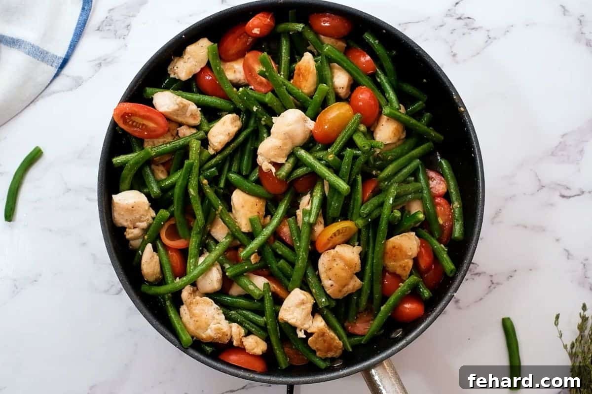 Skillet Chicken Recipe Step 2 Chicken, green beans, and tomatoes sizzling together in a skillet after being sautéed, ready for the next step.