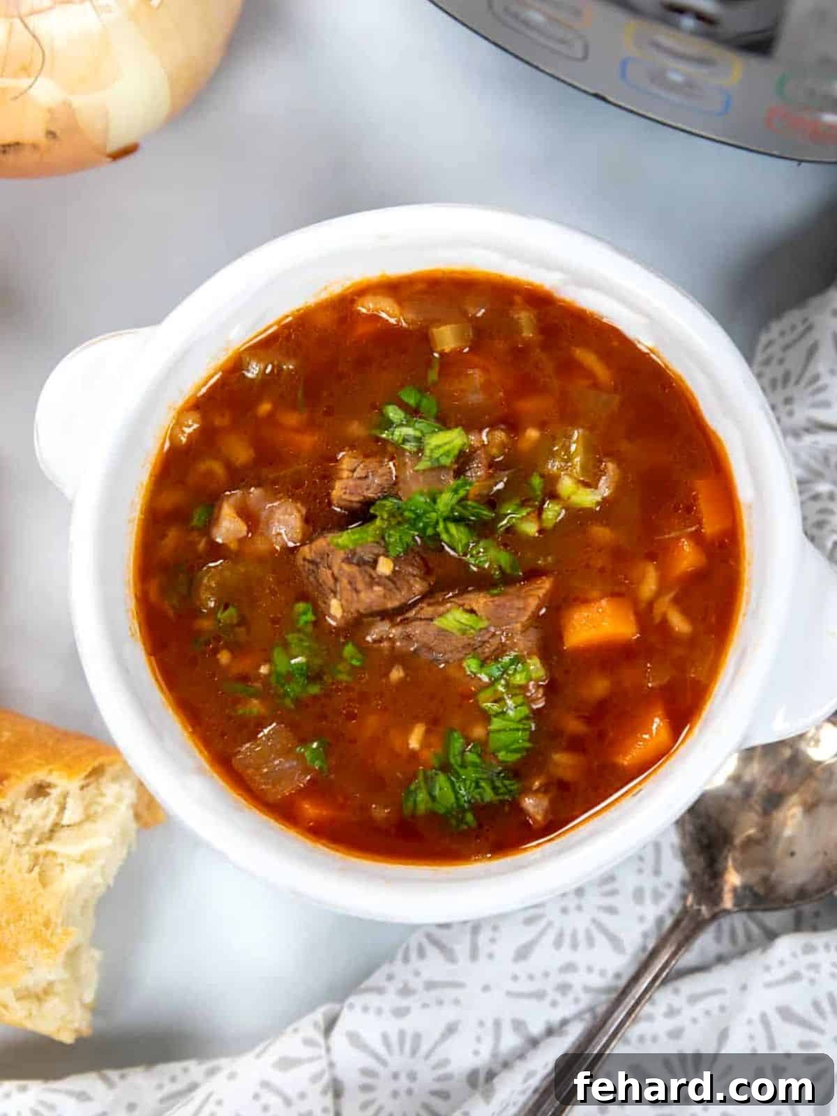 A warm bowl of Instant Pot Beef and Barley Soup, garnished with fresh parsley, sits beside crusty bread on a rustic wooden surface, inviting comfort.