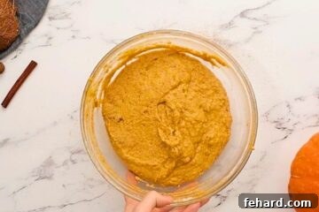 Pumpkin muffin batter after dry and wet ingredients folded together in glass mixing bowl.