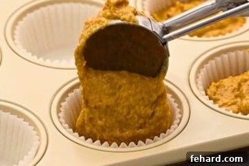 Ice cream scoop scooping pumpkin muffin batter into muffin tin.