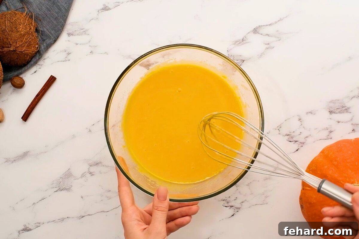 Pumpkin puree, coconut milk, cooled coconut oil, egg, and vanilla extract whisked together in a large mixing bowl, forming a smooth wet mixture.