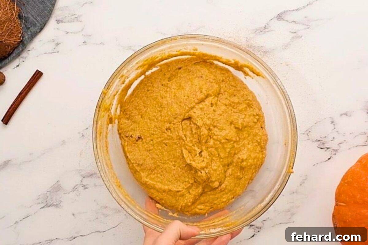 Pumpkin muffin batter in a glass mixing bowl after dry and wet ingredients have been gently folded together, showing a slightly lumpy consistency.