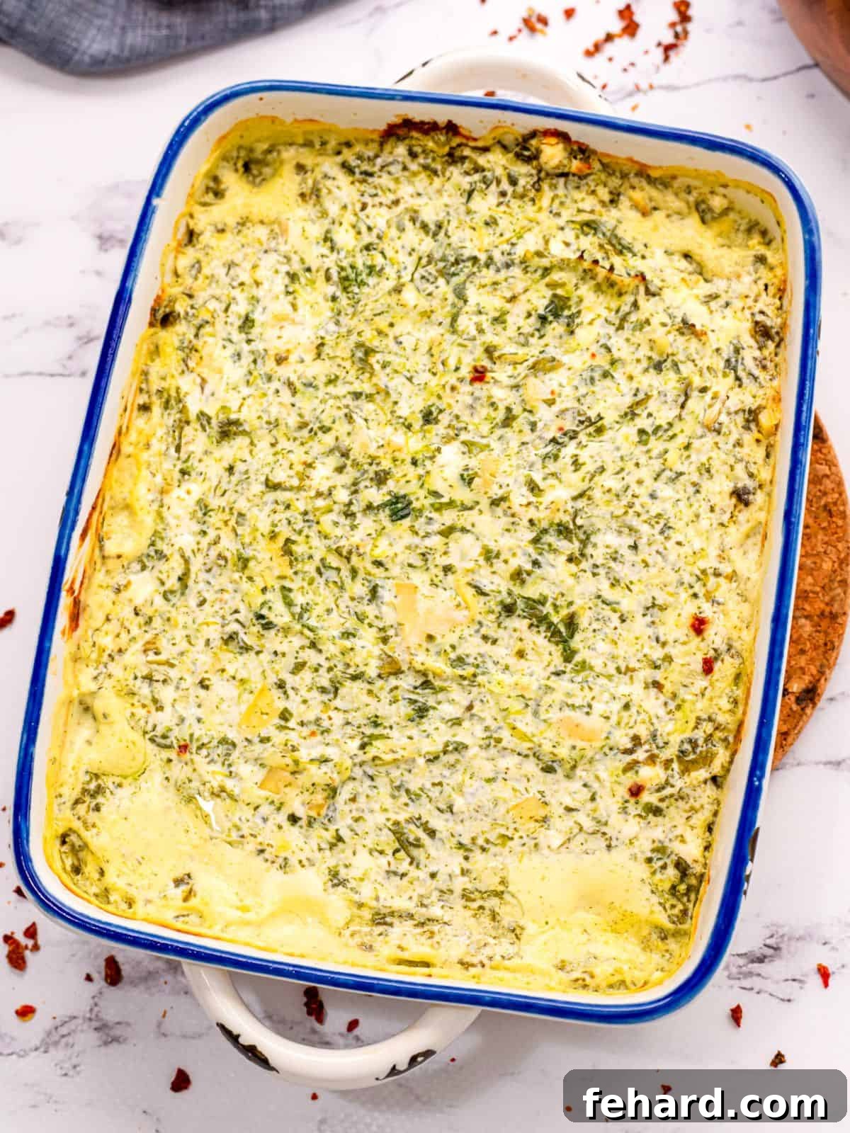 Baked Spinach Artichoke Dip in white baked dish.