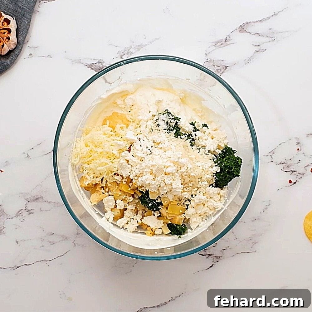 All ingredients for Spinach Artichoke Dip mixed together in a clear mixing bowl.