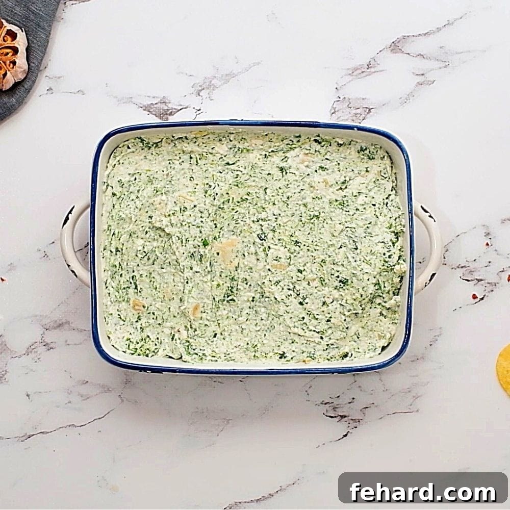 Unbaked spinach artichoke dip spread evenly in a baking dish.