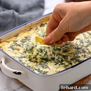 Scooping out spinach dip from a baking dish with a chip.
