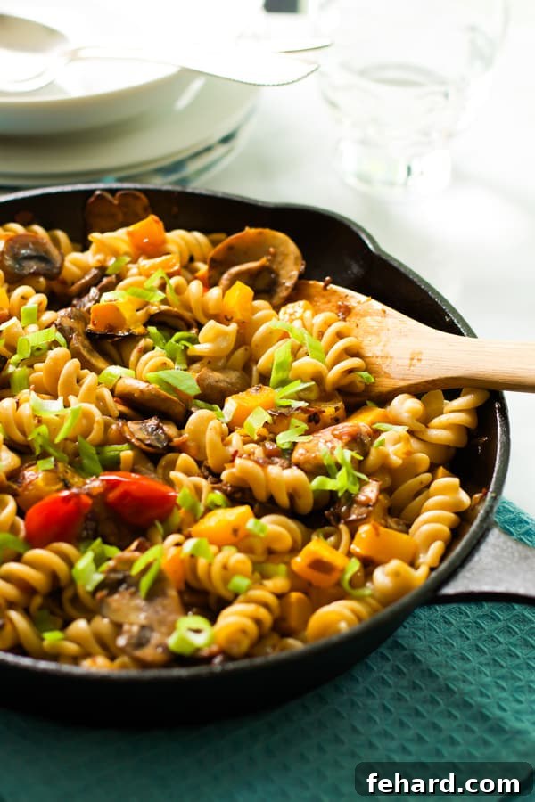A serving of fusilli with mushroom and roasted butternut squash being spooned from a larger dish.