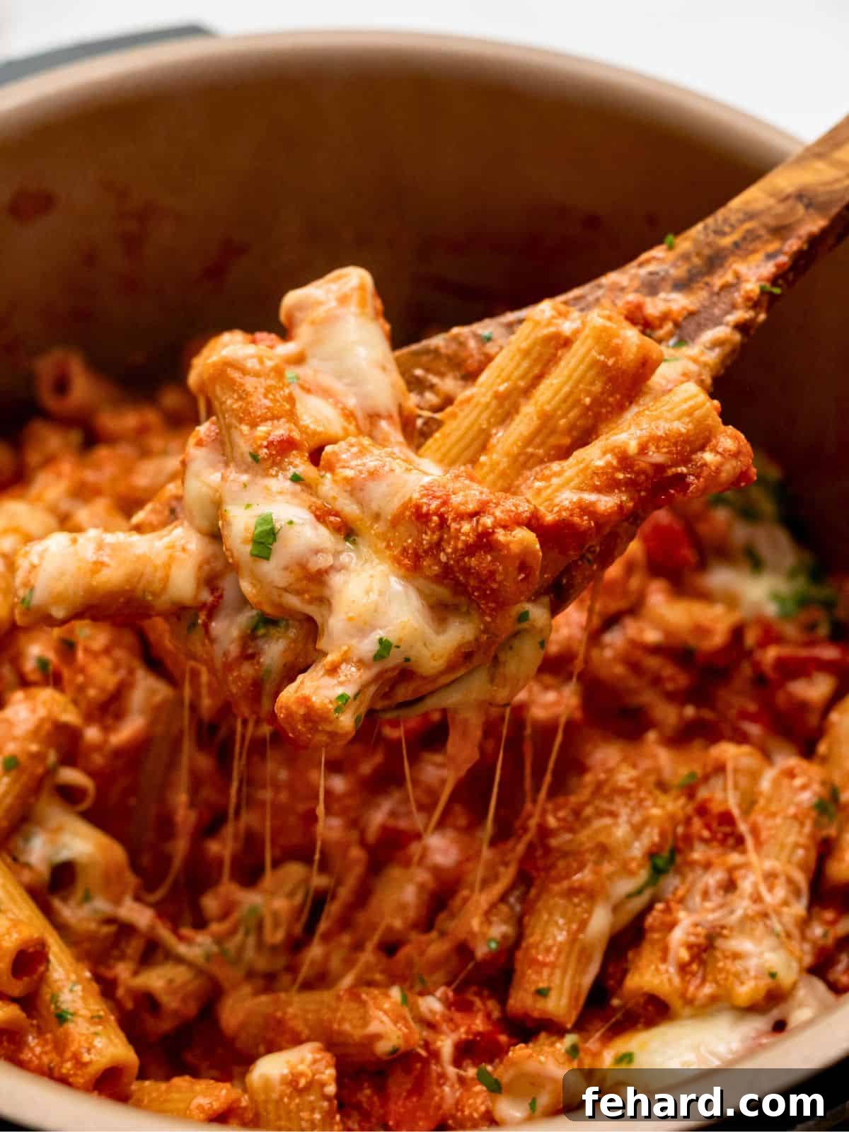 Wooden spoon scooping out cheesy pasta coated in rich tomato sauce from inside Instant Pot, highlighting its creamy texture.