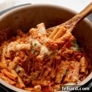 Wooden spoon scooping out cheesy ziti from inside Instant Pot, showcasing the texture.