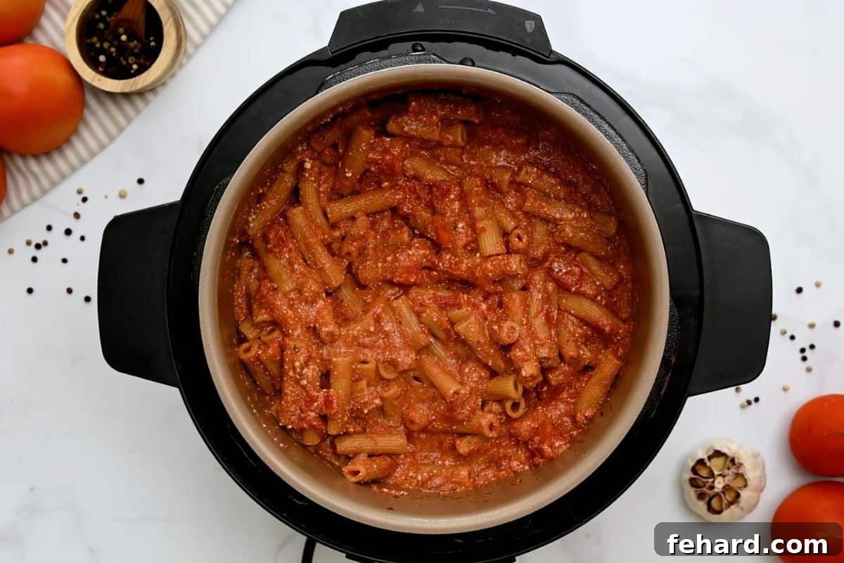 Ziti cooked with tomato sauce and ricotta being stirred together inside the inner pot of an electric pressure cooker, showcasing the transformation.
