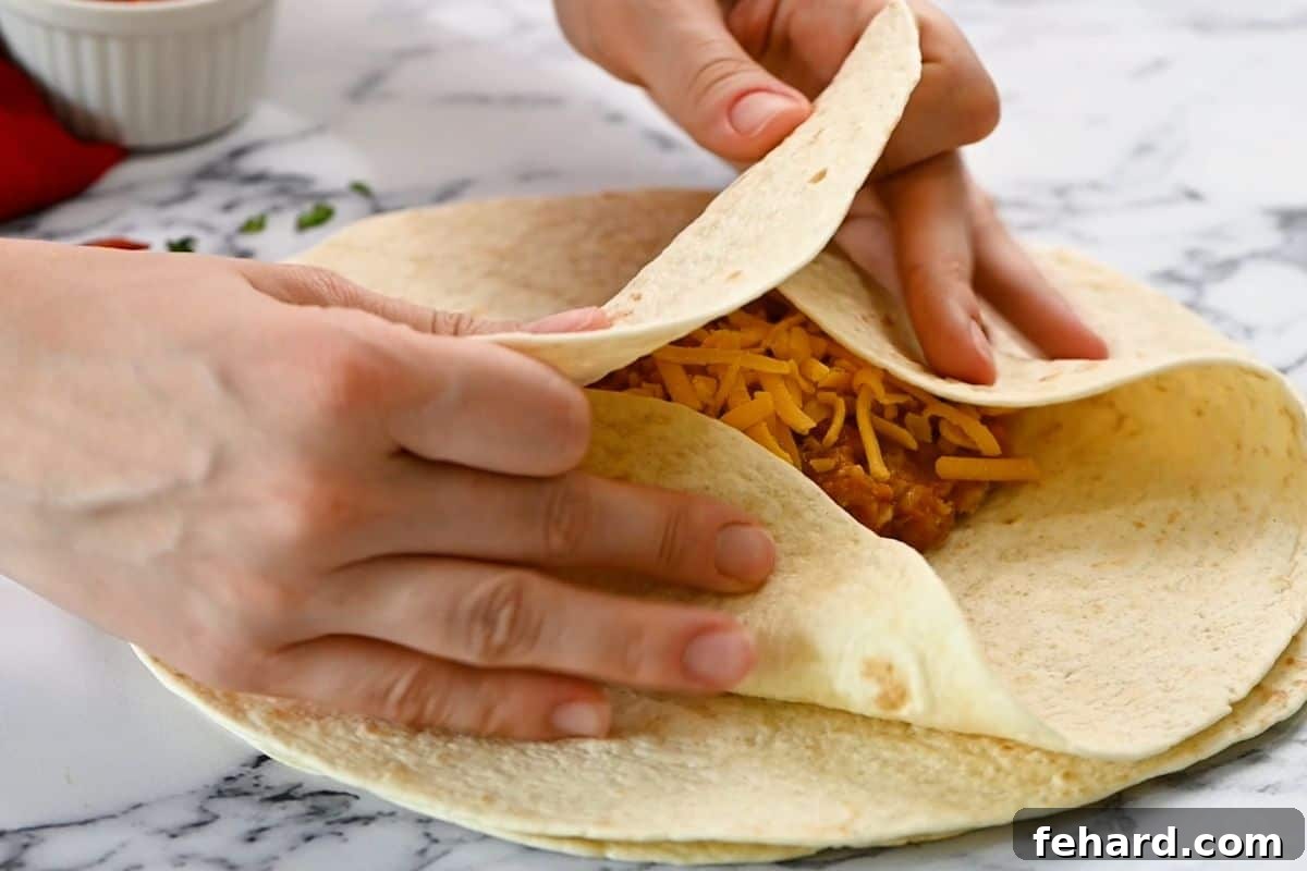 how to roll burrito Hands demonstrating the folding technique for rolling a burrito, tucking in the sides over the filling.