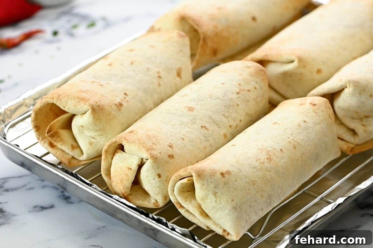 Vegetarian Bean Burritos Several baked refried bean burritos resting on a wire rack over a baking sheet, showcasing their golden-brown, crispy exteriors.