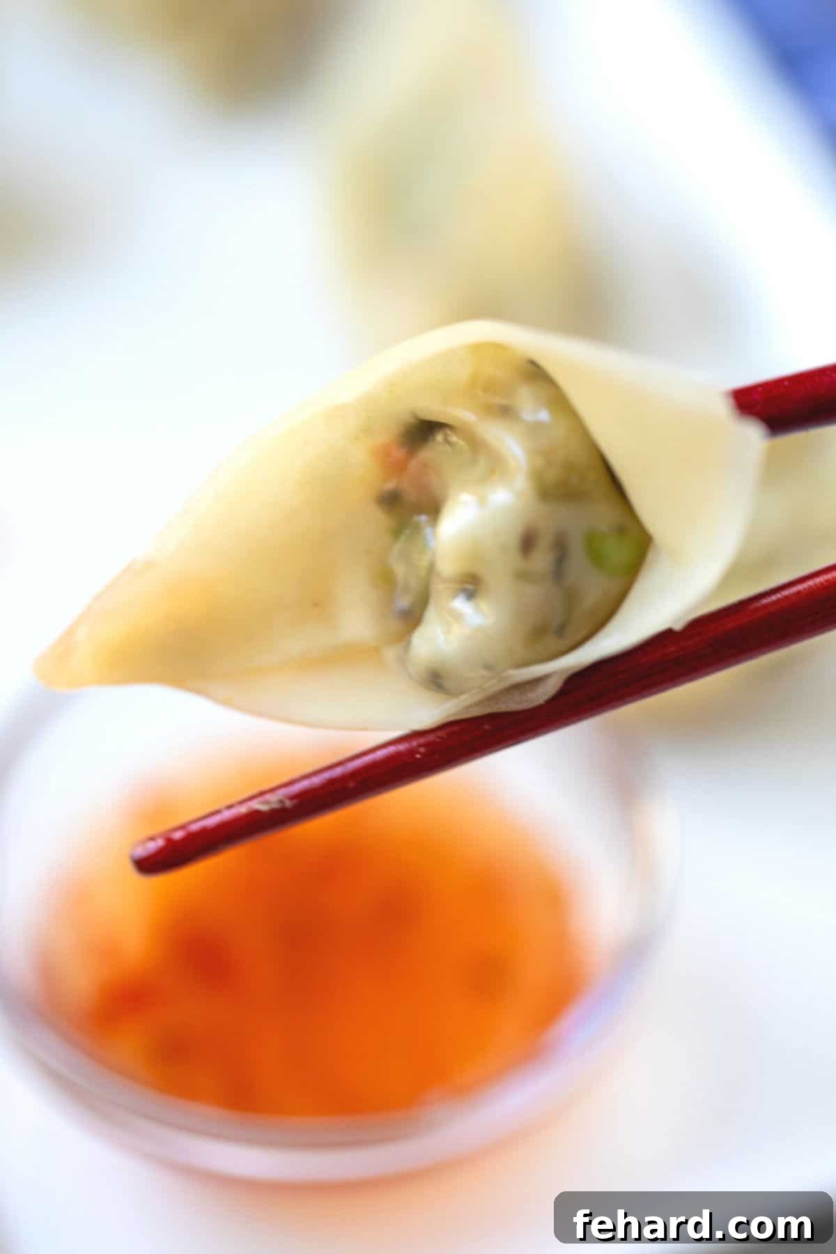 A golden-brown homemade potsticker held by wooden chopsticks, about to be dipped into sweet chili sauce, highlighting its crispy texture and delicious appeal.