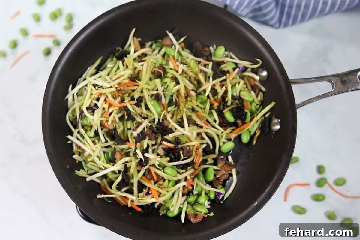 A vibrant mix of sautéed vegetables, including broccoli slaw, mushrooms, and edamame, simmering in a pan, ready to become the delicious filling for potstickers.