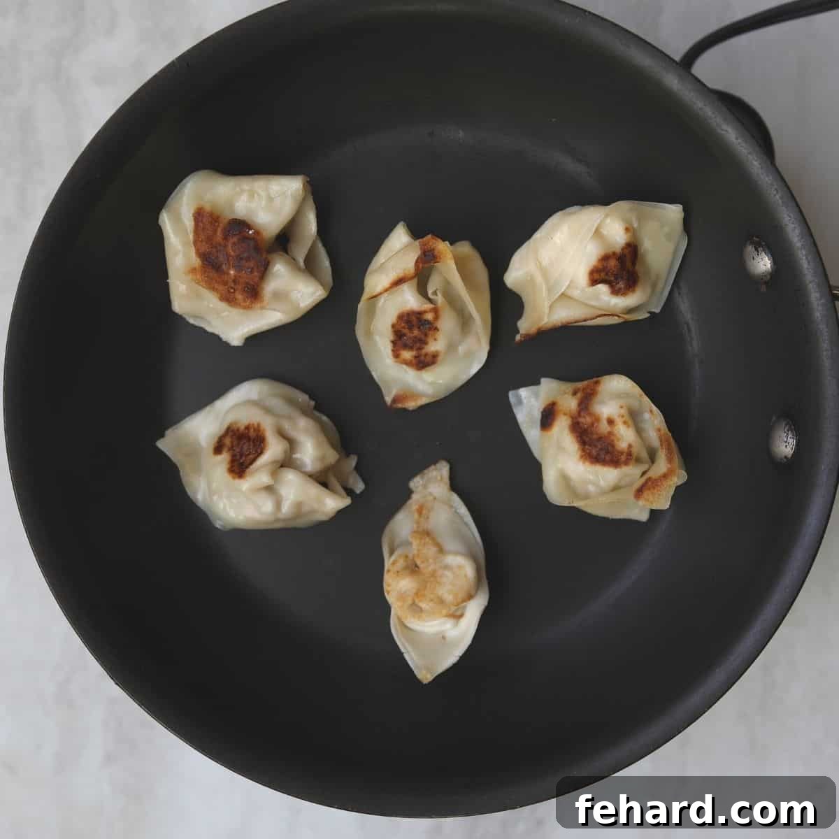 Close-up of pan-fried wonton wrappers (potstickers) sizzling in a skillet, showcasing their beautifully browned and crispy bottoms.