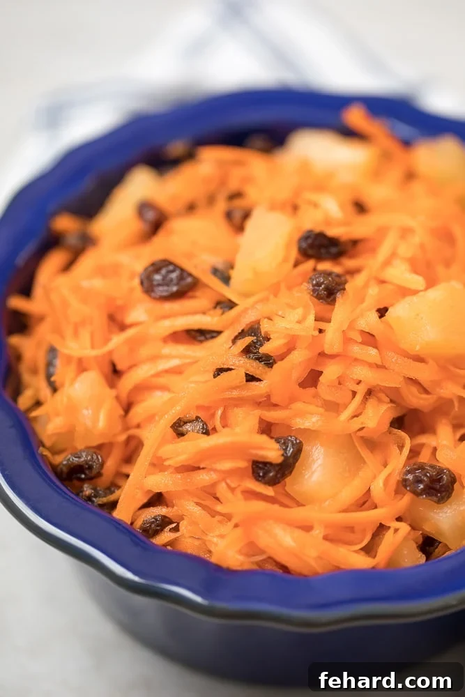 A vibrant Carrot Raisin Salad with pineapple in a beautiful blue serving bowl, ready to be enjoyed. The salad is a healthy and refreshing side dish.