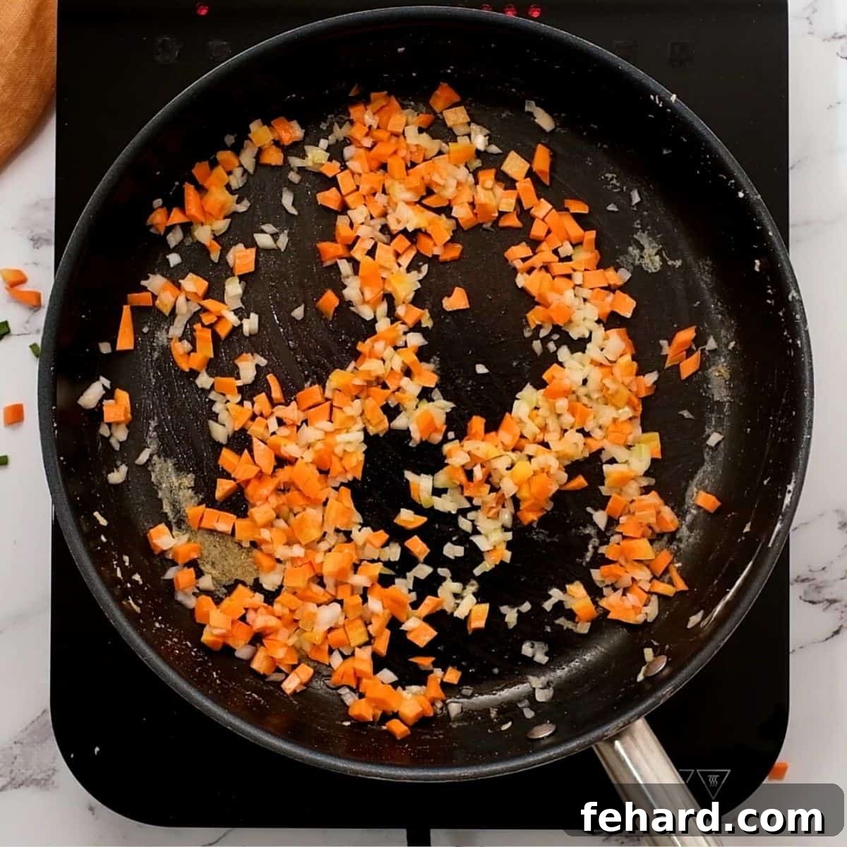 Carrots, onions, and garlic being sautéed in a large pan for fried rice.