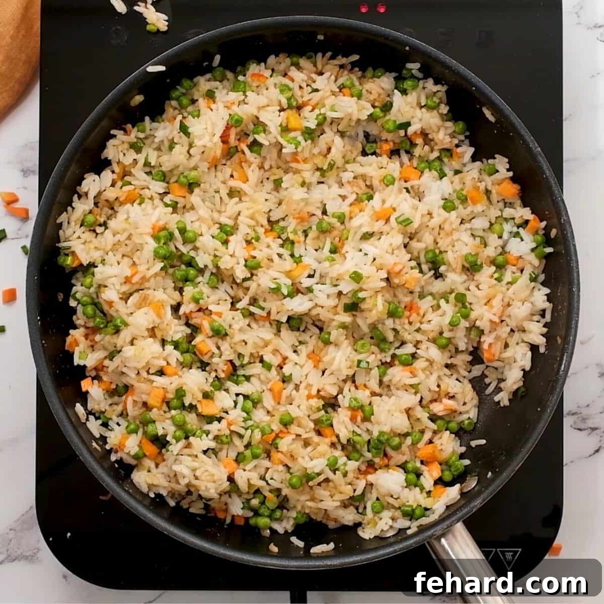 Cold rice, carrots, and peas frying in a large skillet, absorbing the flavors.