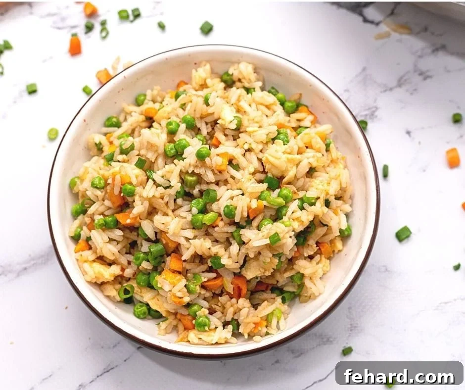A bowl of freshly made homemade fried rice with brown rice, peas, and green onions.