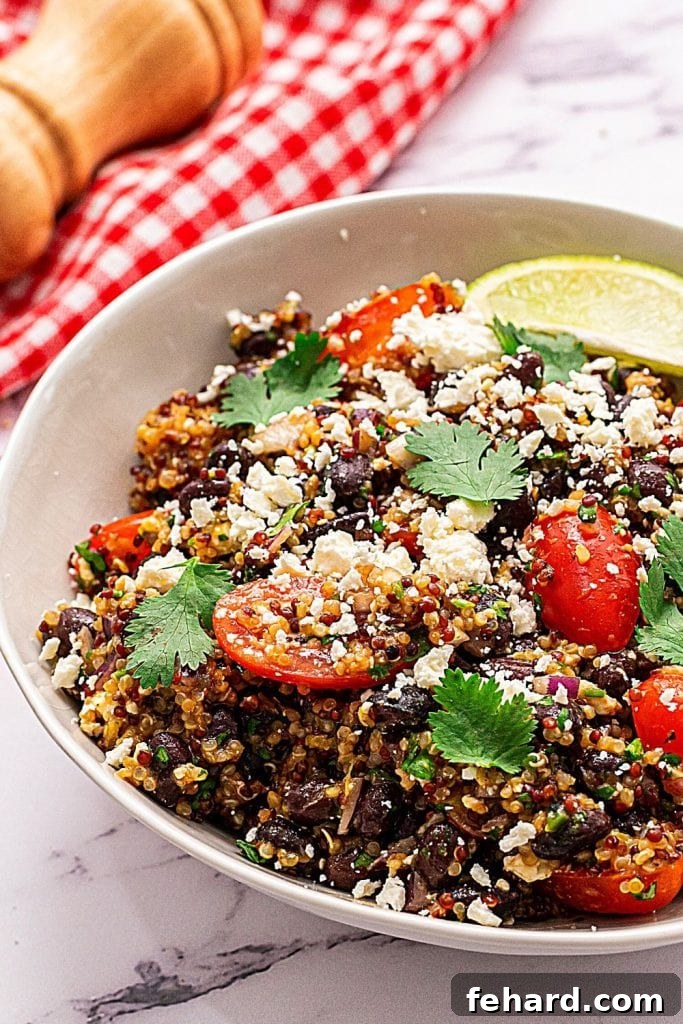 Mexican Quinoa Salad Recipe Gluten Free Mexican Quinoa Salad in white bowl topped with feta and cherry tomatoes, showcasing a vibrant mix of ingredients like quinoa, black beans, tomatoes, and cilantro with a zesty lime dressing.