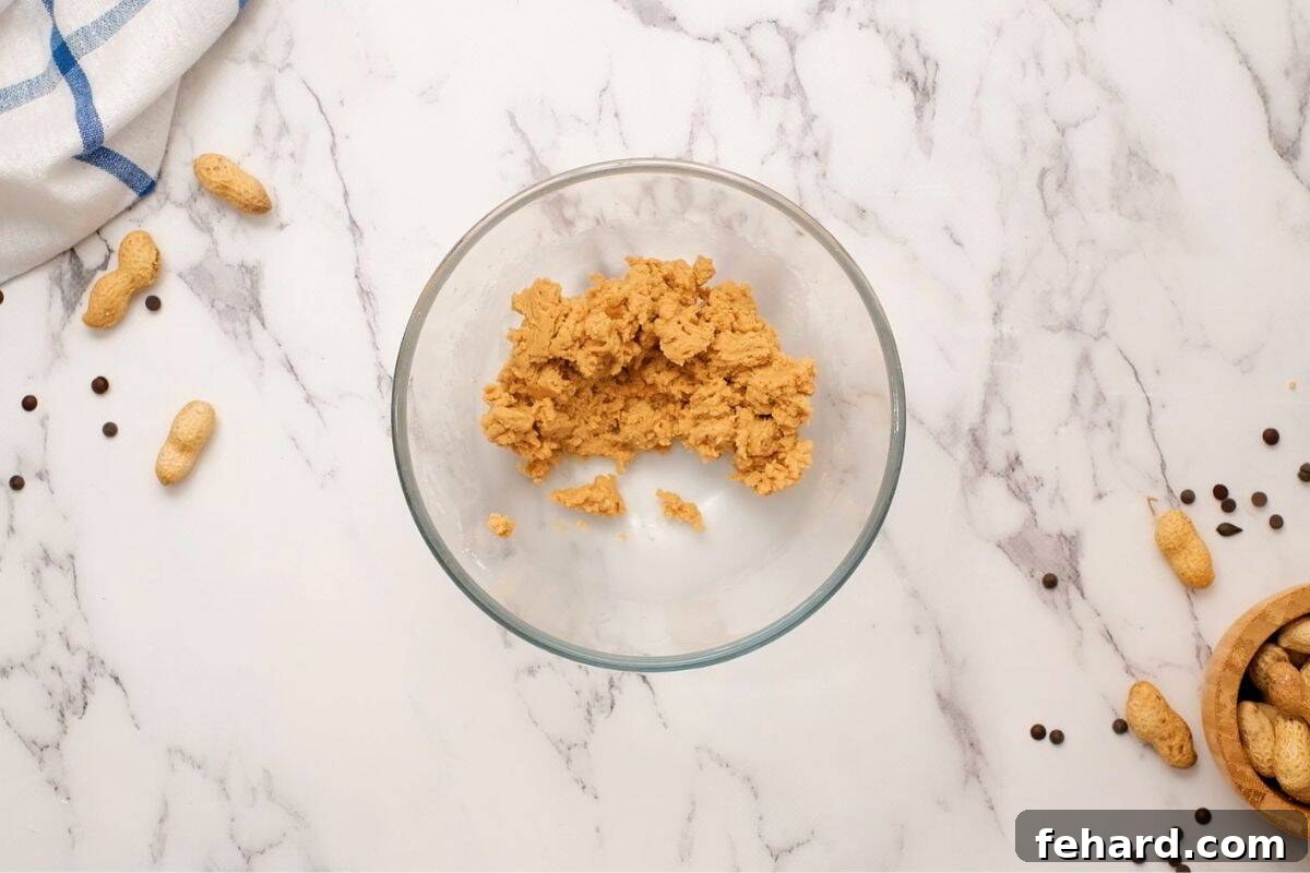 Peanut butter, powdered sugar, vanilla, and salt mixed together in a glass mixing bowl, showcasing the ideal dough-like consistency.