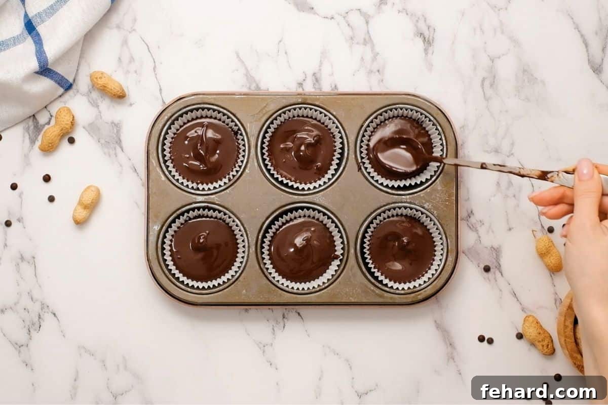 Spoon melted chocolate over peanut butter mixture in muffin tin to form chocolate peanut butter cups. The final layer is being applied.