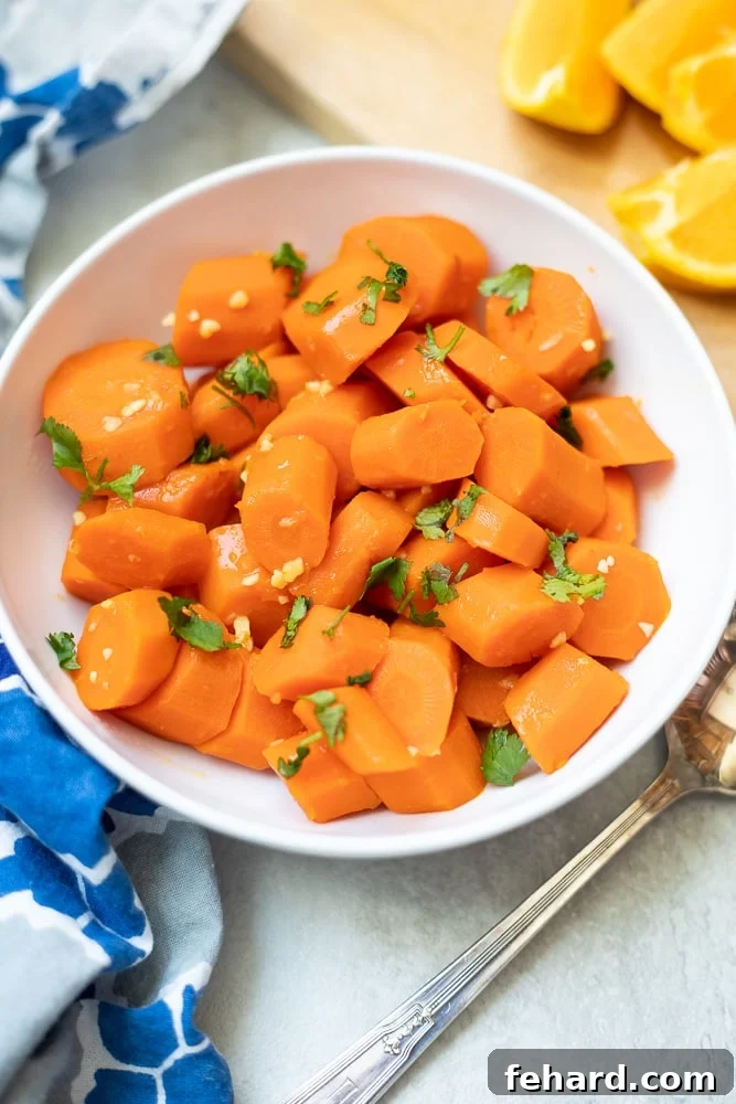 Quick & Sweet Glazed Carrots 2 A bowl of beautifully glazed carrots, garnished and ready to serve, next to fresh orange slices.